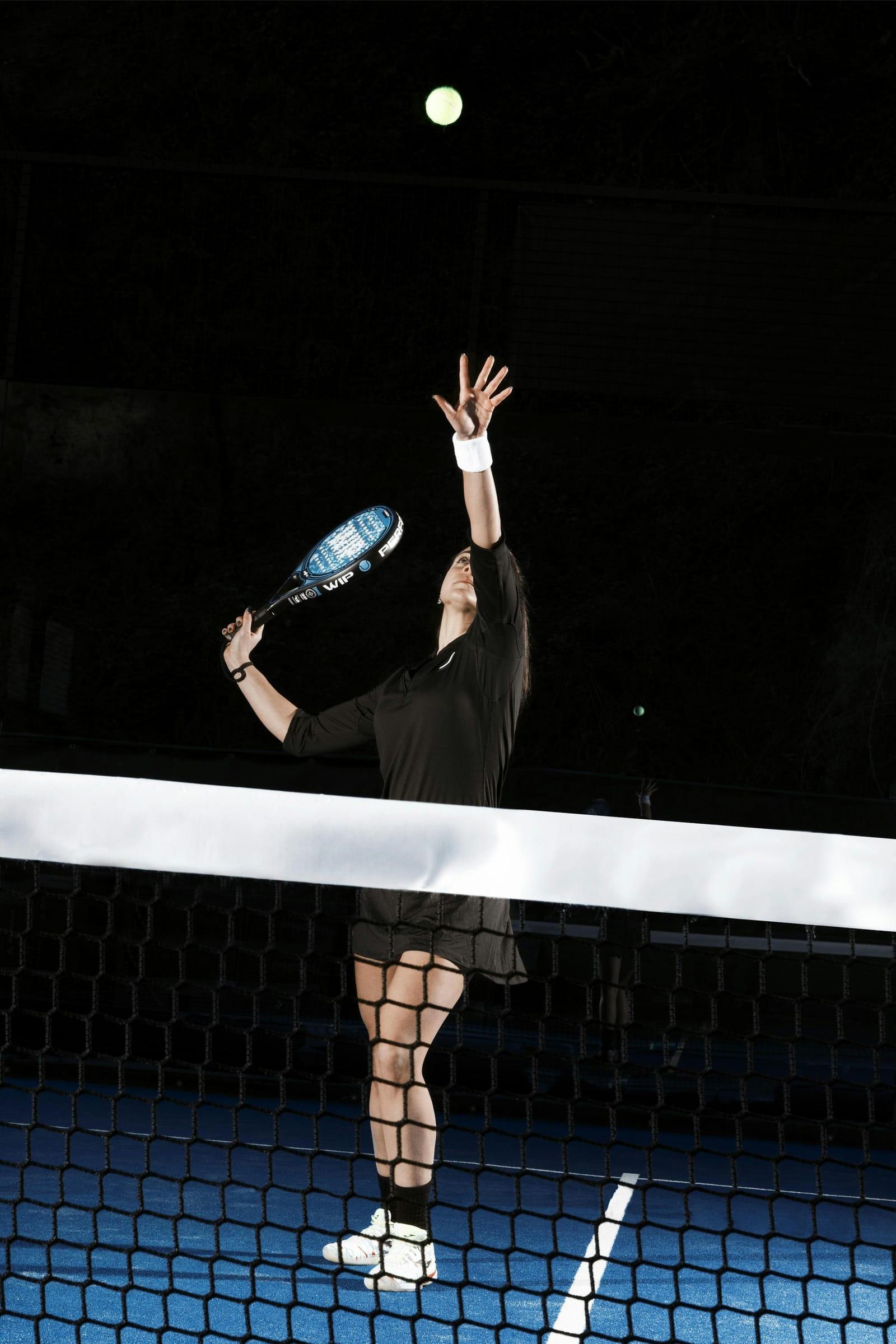 Padel player reaching up for an overhead smash under floodlights